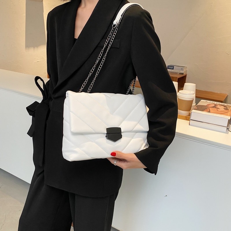 Borsa trapuntata bianca con tracolla a catena e chiusura nera, portata sul fianco con un blazer nero
