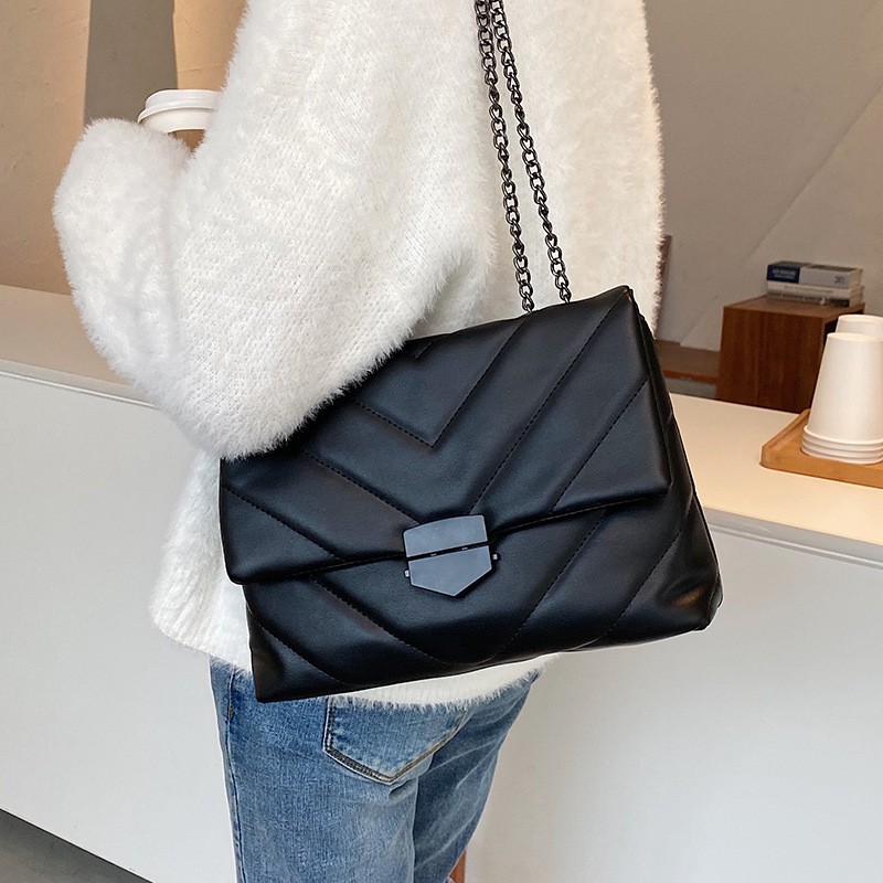Borsa trapuntata nera con cuciture a V sulla patta, portata sul fianco sopra un maglione bianco