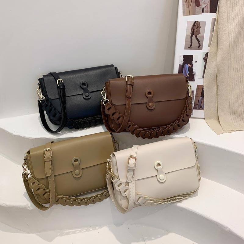 Quattro borse a tracolla nera, marrone, cachi e bianco panna su un gradino bianco, con patta e fascia intrecciata