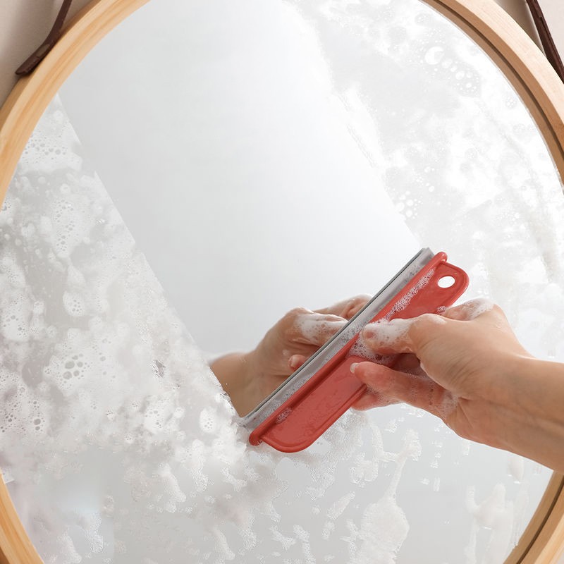 Tergivetro rosso che toglie la schiuma da uno specchio rotondo con cornice in legno