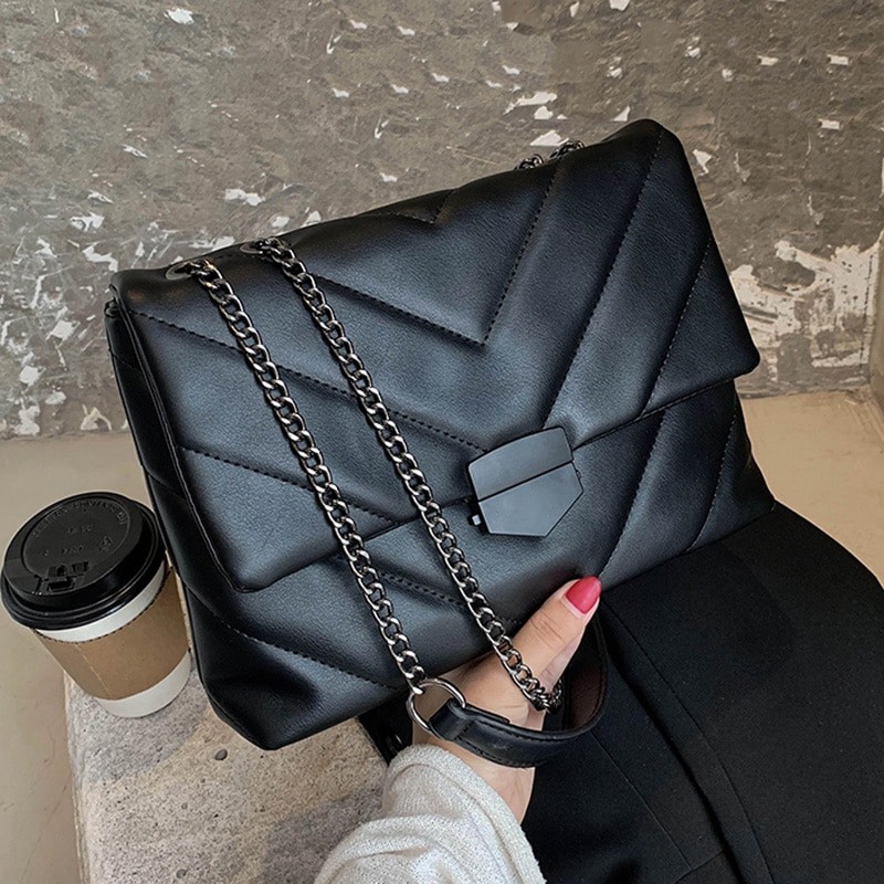 Primo piano della borsa trapuntata nera con la catena appoggiata davanti e la chiusura nera