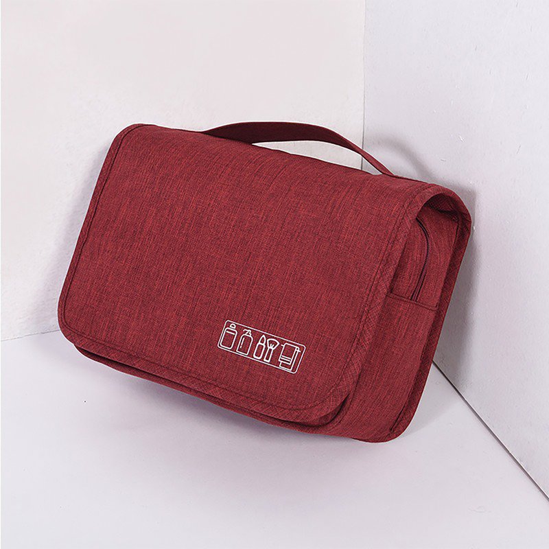 Beauty case rosso scuro chiuso, appoggiato a un angolo, con maniglia
